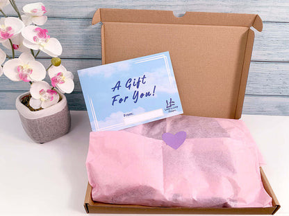 Gift box - cardboard with pink recycled tissue paper gift wrap and heart sticker closure. Gift insert card that has blue sky and clouds reads A Gift for You! 