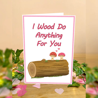 Cute Mushroom / Toadstool woodland theme Greetings card for 5 year wood anniversary or valentines. White card of 2 toadstool mushrooms on top of wooden log smiling together with two hearts floating just above them. Wording I wood do Anything for You in red text above image Red and white polkadot spotty thin border. Flower petals scattered around card placed on a wooden table with leaves on