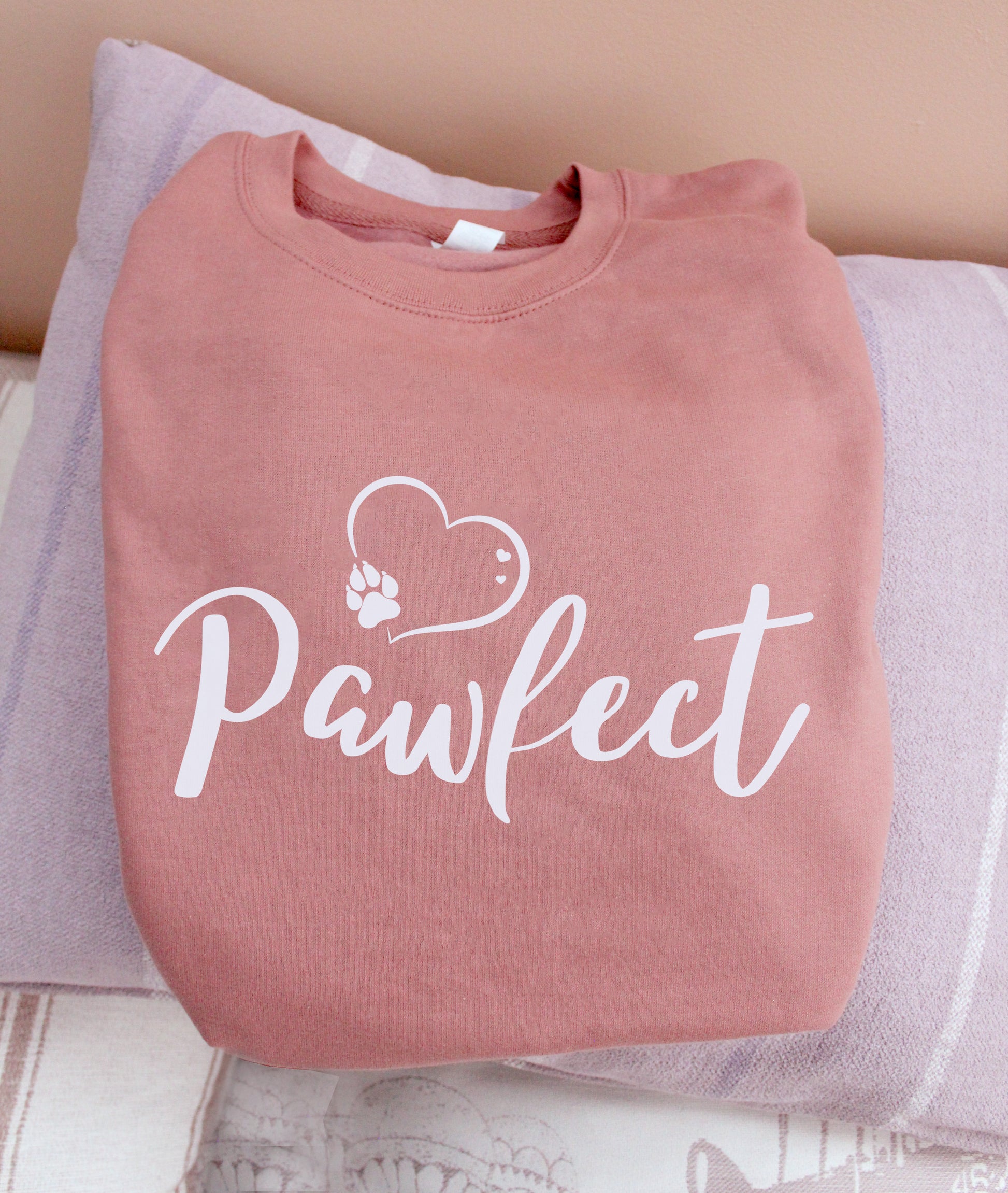 Folded Dusty pink colour relaxed fit long sleeve sweatshirt . Slogan sweater design wording Pawfect in white font and white heart outline above with dog paw print within outline.