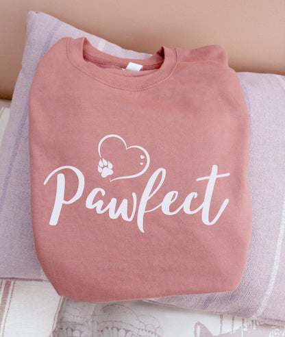 Folded Dusty pink colour relaxed fit long sleeve sweatshirt . Slogan sweater design wording Pawfect in white font and white heart outline above with dog paw print within outline.
