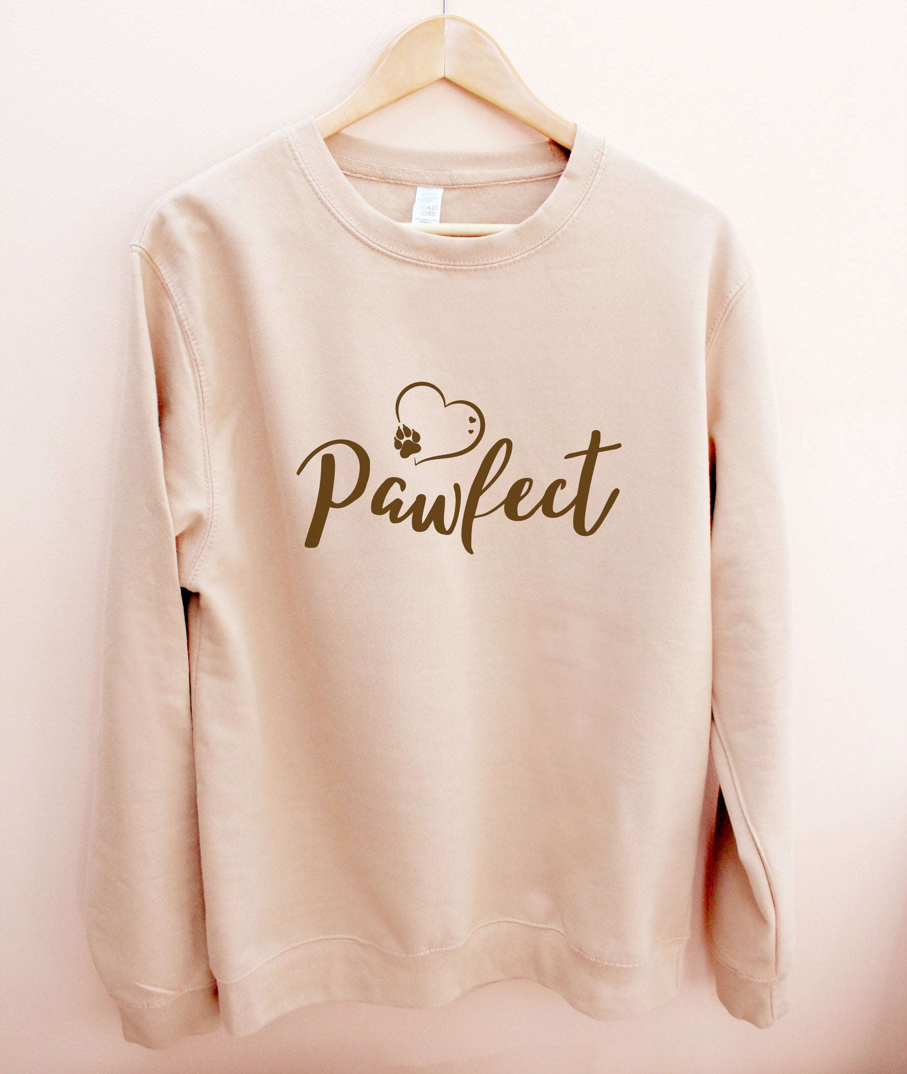 Beige / Caramel colour relaxed fit long sleeve sweatshirt on wooden hanger Slogan sweater design wording Pawfect in brown font and brown heart outline above with dog paw print within outline.